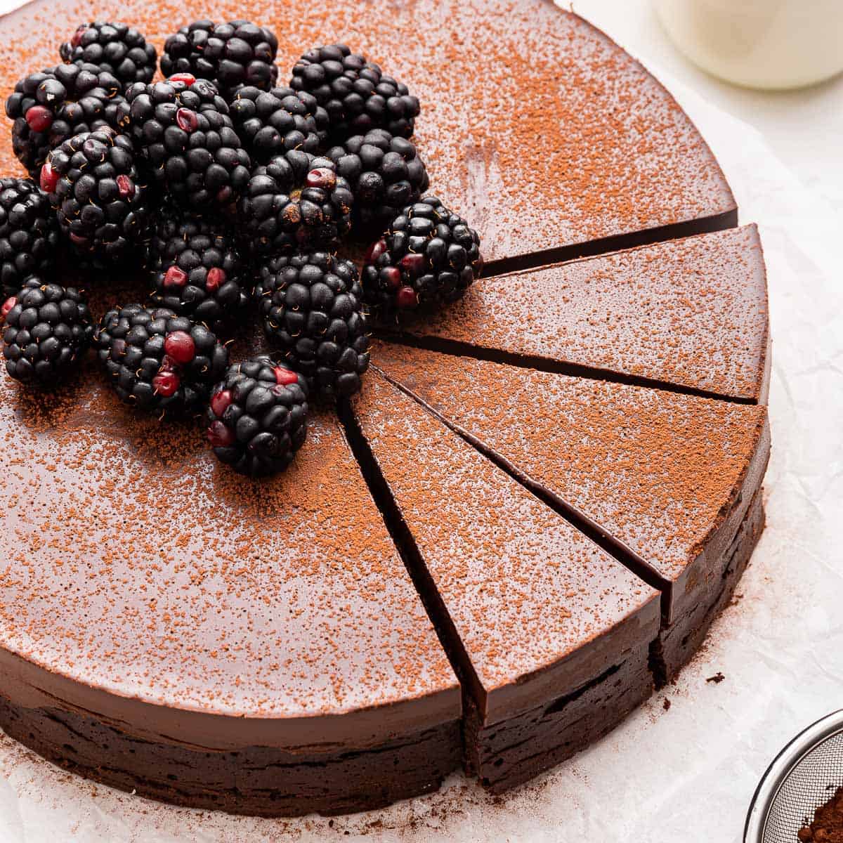 A flourless chocolate cake cut into slices and topped with fresh blackberries.