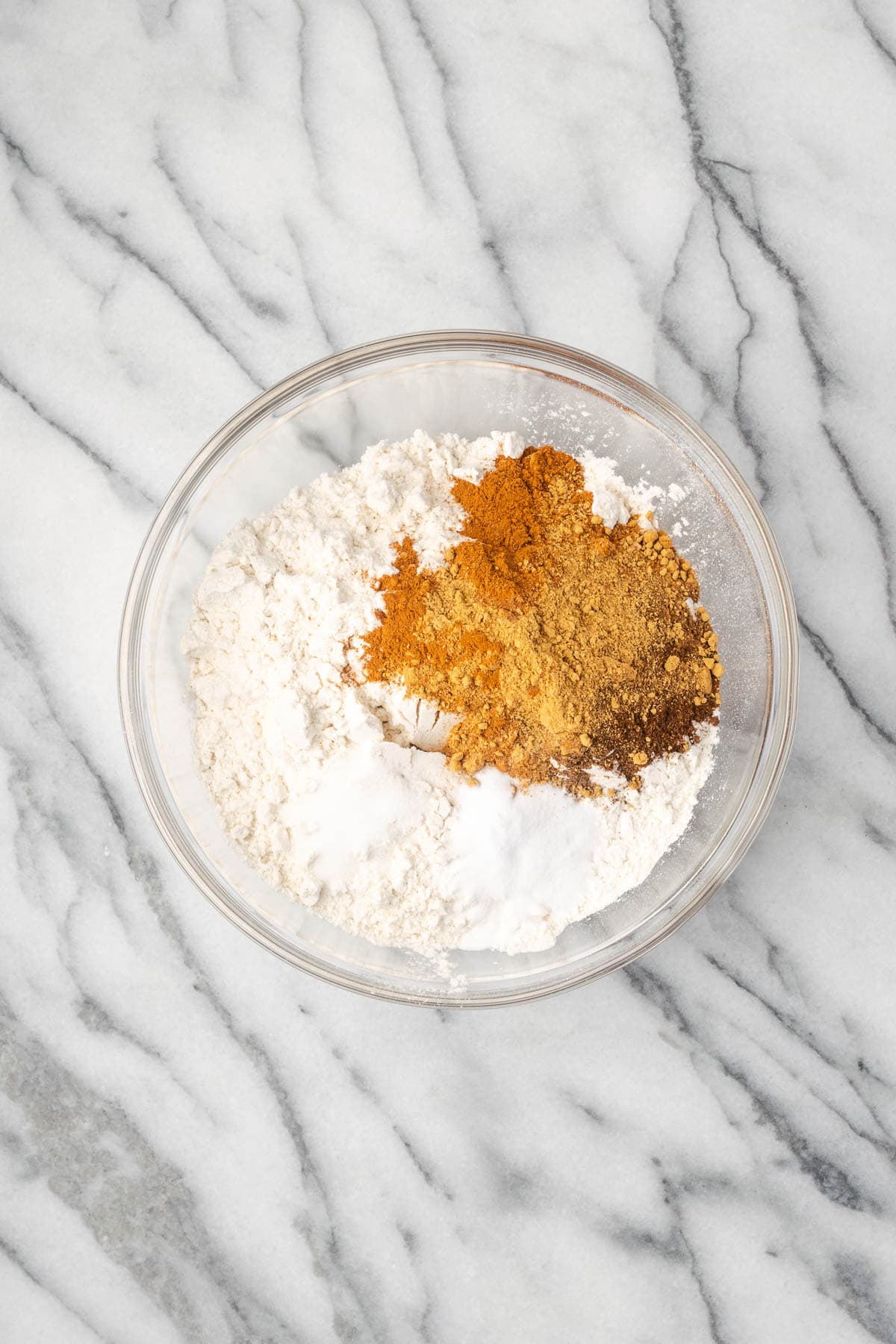 Flour, baking soda, salt and spices combined in a glass mixing bowl.