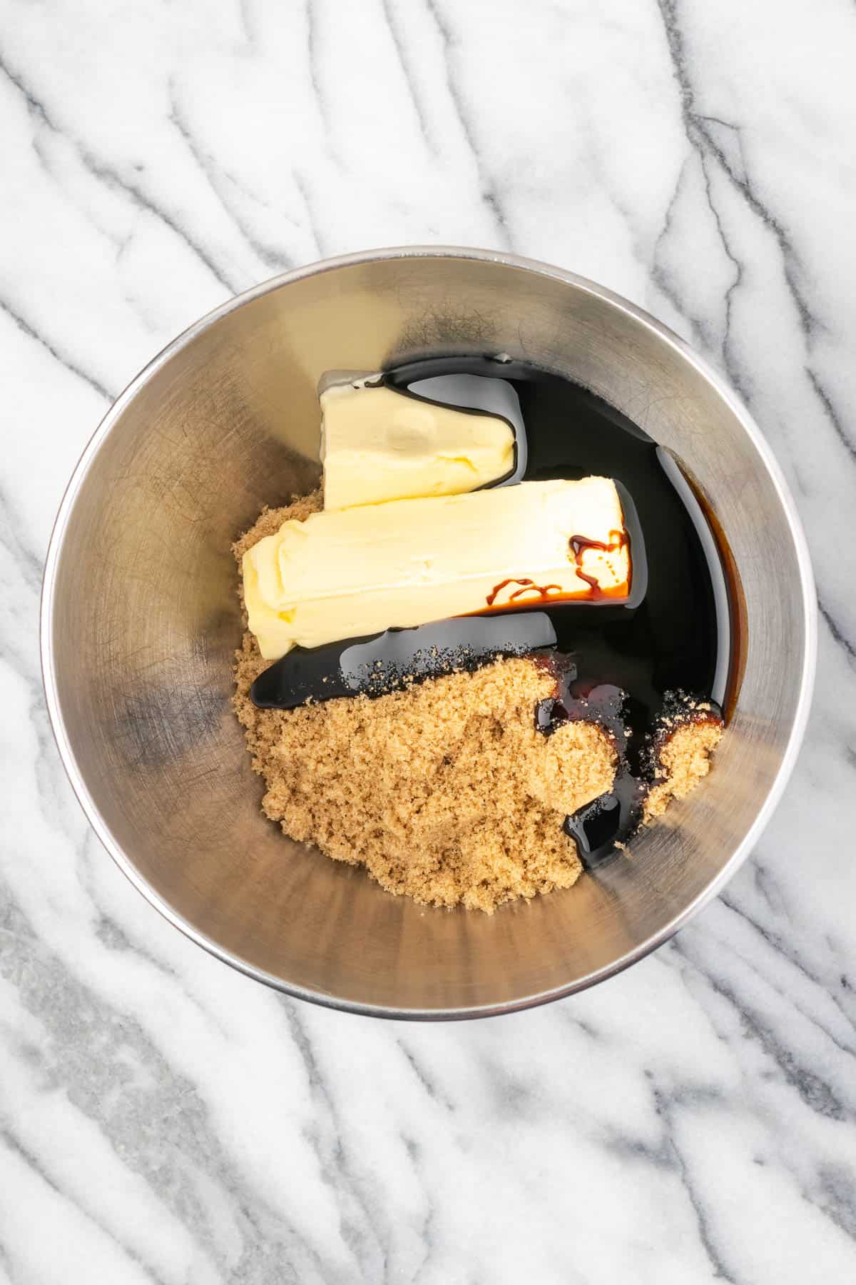 Butter, brown sugar and molasses being creamed in a large metal bowl.