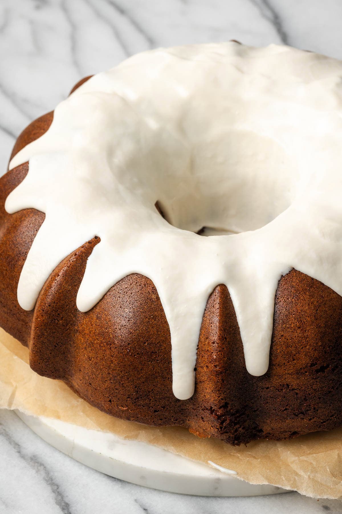 A gingerbread bundt cake covered with white chocolate ganache sitting on a small marble board.