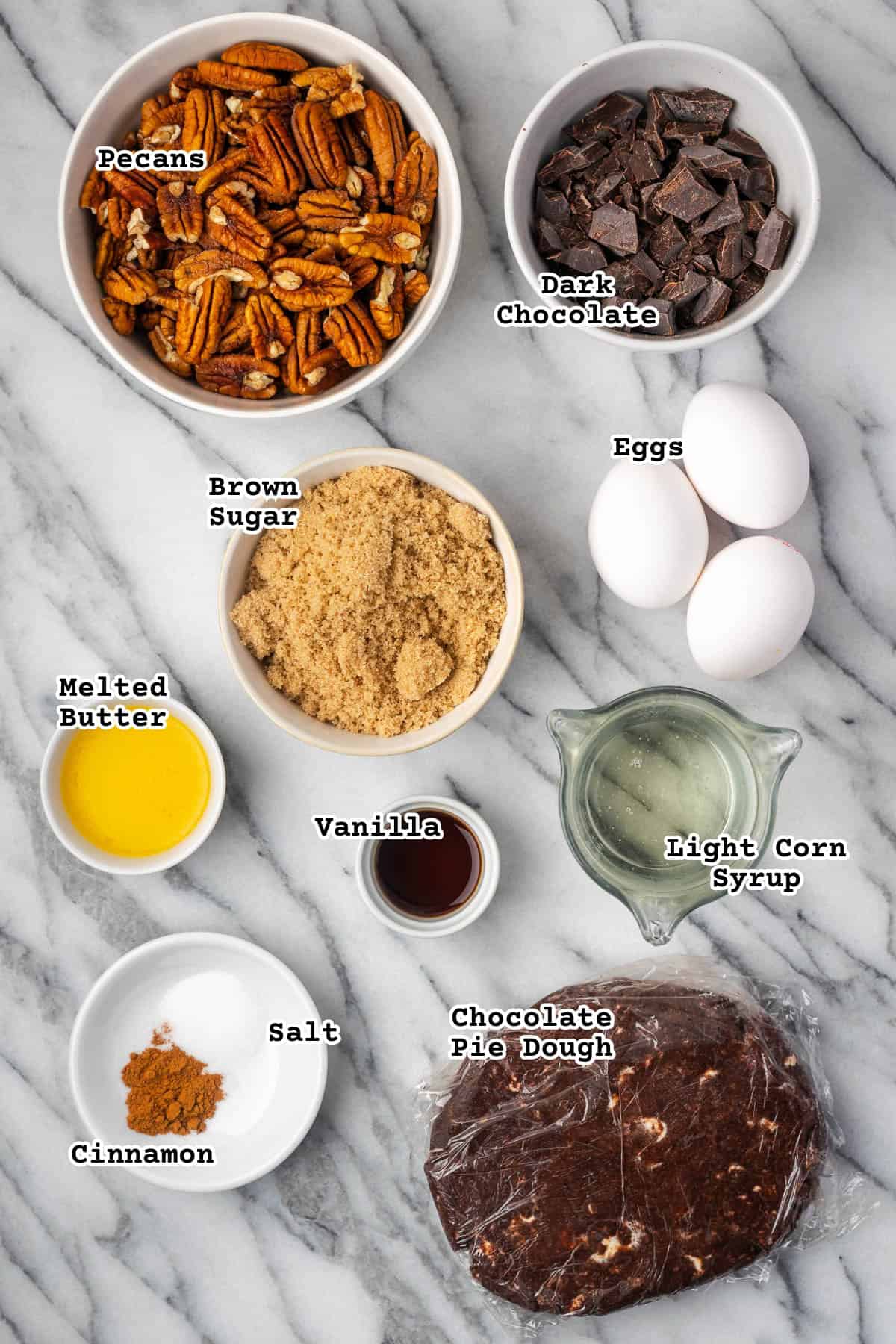 Ingredients for a chocolate pecan pie sitting on a marble counter.