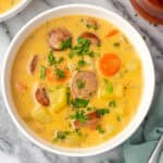 A bowl of kielbasa potato soup sitting on a marble counter.