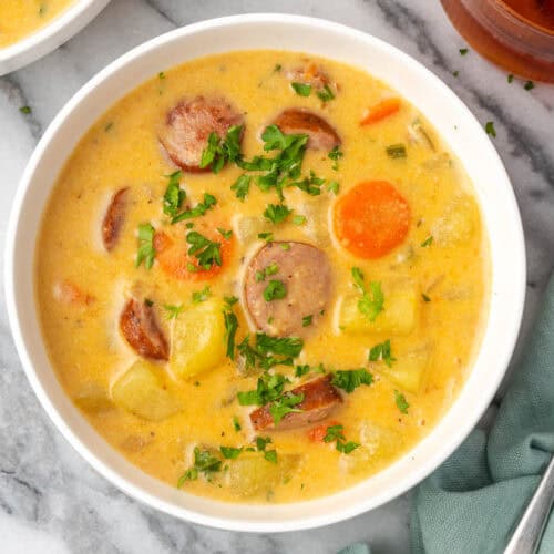A bowl of kielbasa potato soup sitting on a marble counter.