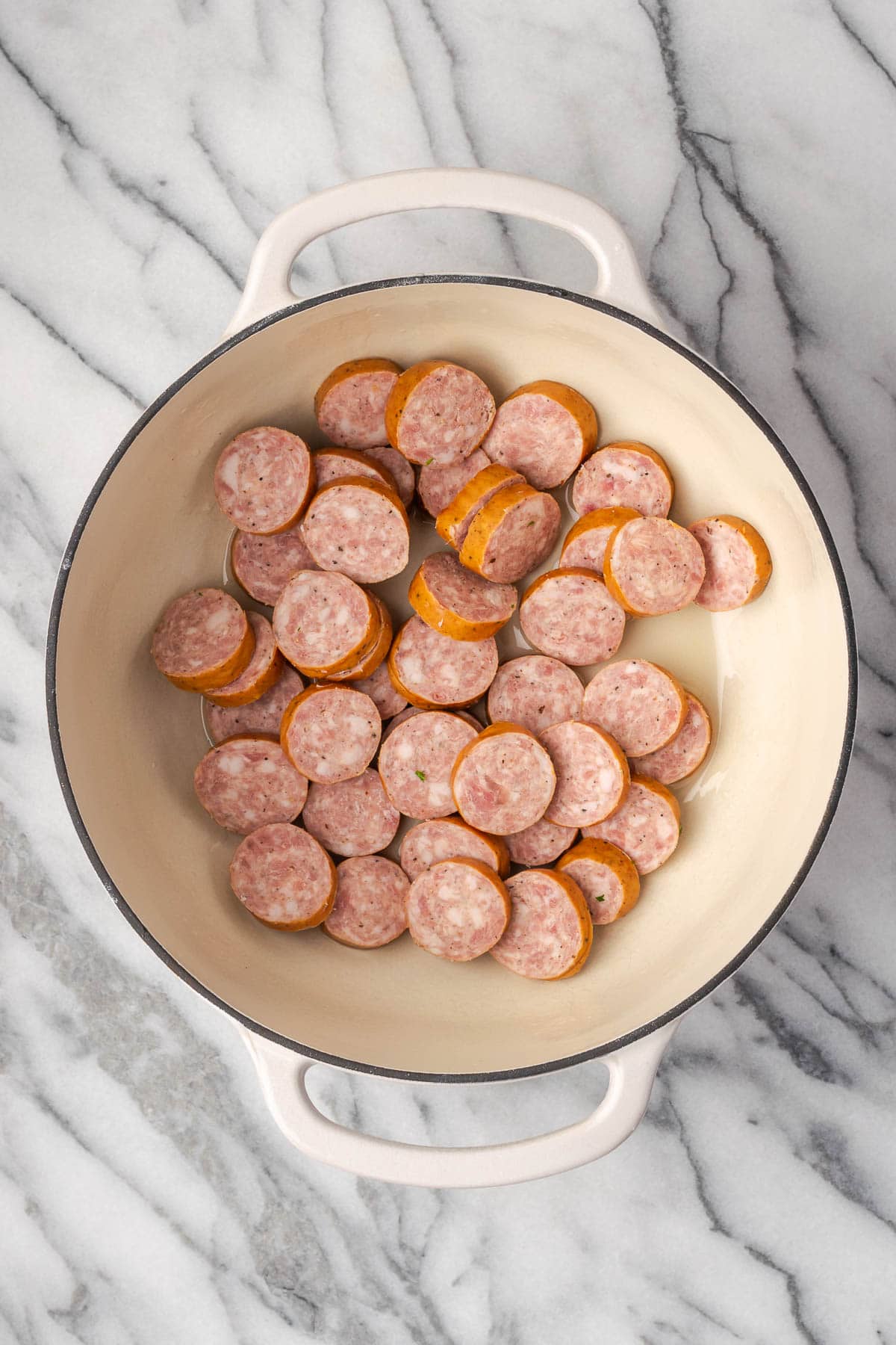Kielbasa coins being cooked in a large dutch oven pot. 