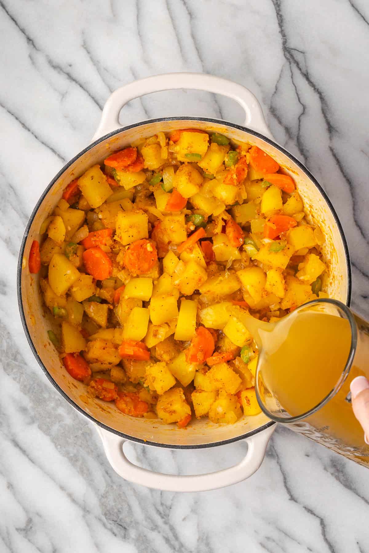 Chicken broth being poured into the pot with the cooked vegetables. 