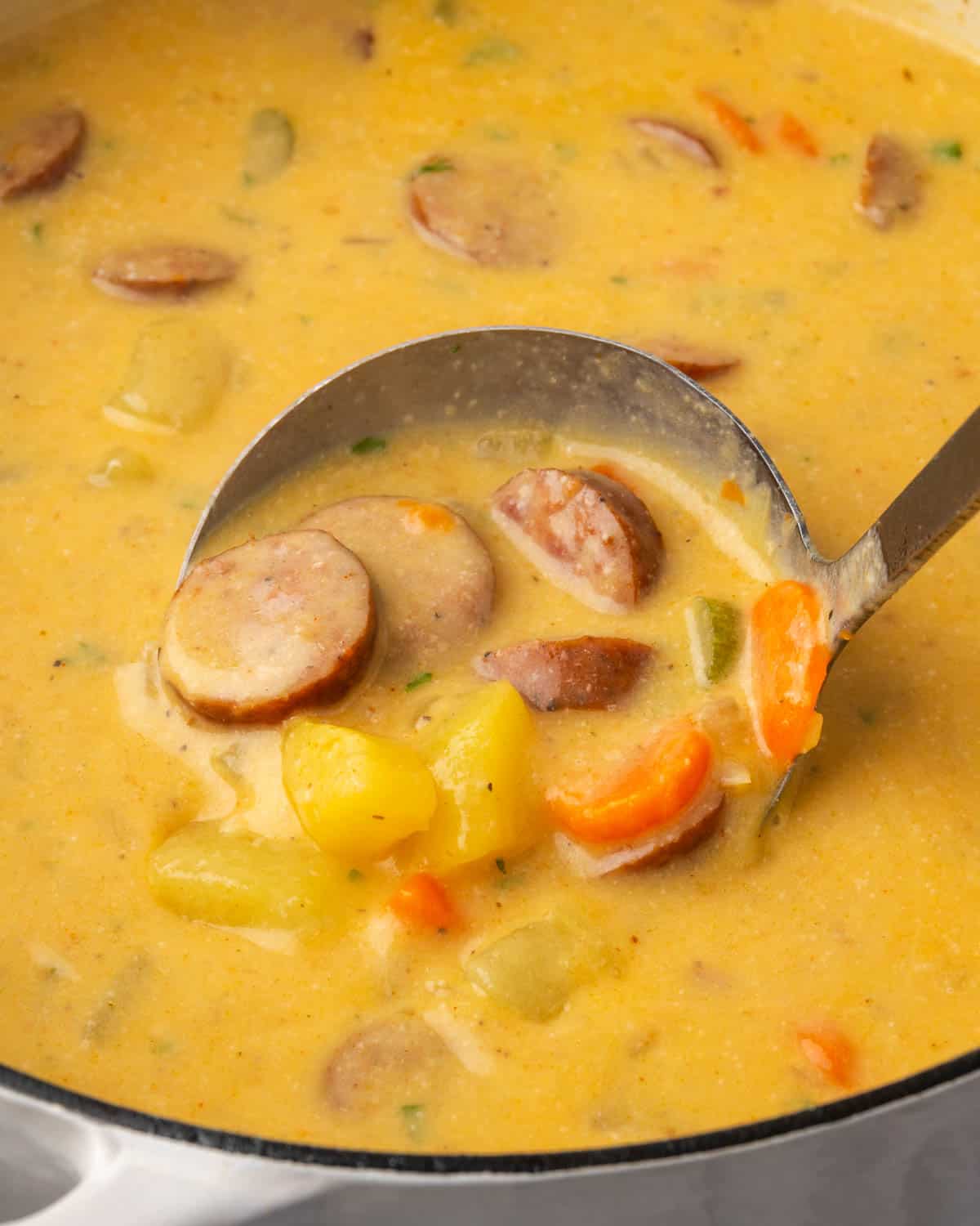 A ladle scooping up a serving of kielbasa potato soup from a large pot. 