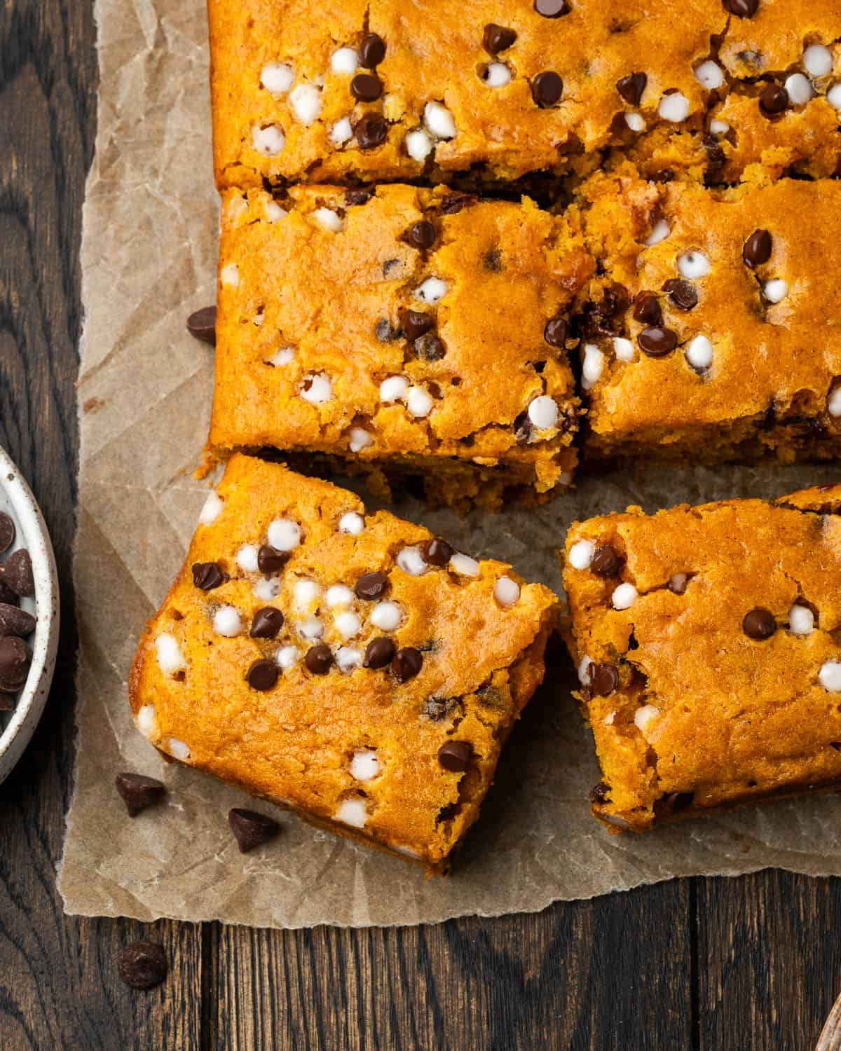 A freshly baked pumpkin chocolate chip cake cut into squares sitting on a wood table. 