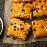 A gluten free pumpkin chocolate chip cake cut into squares sitting on a wood table.