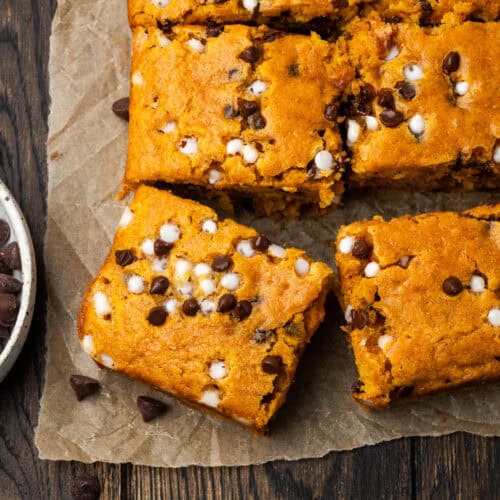 A gluten free pumpkin chocolate chip cake cut into squares sitting on a wood table.