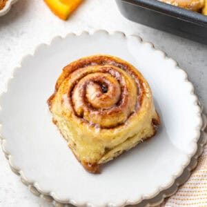 An orange cinnamon roll served on a small dessert plate.