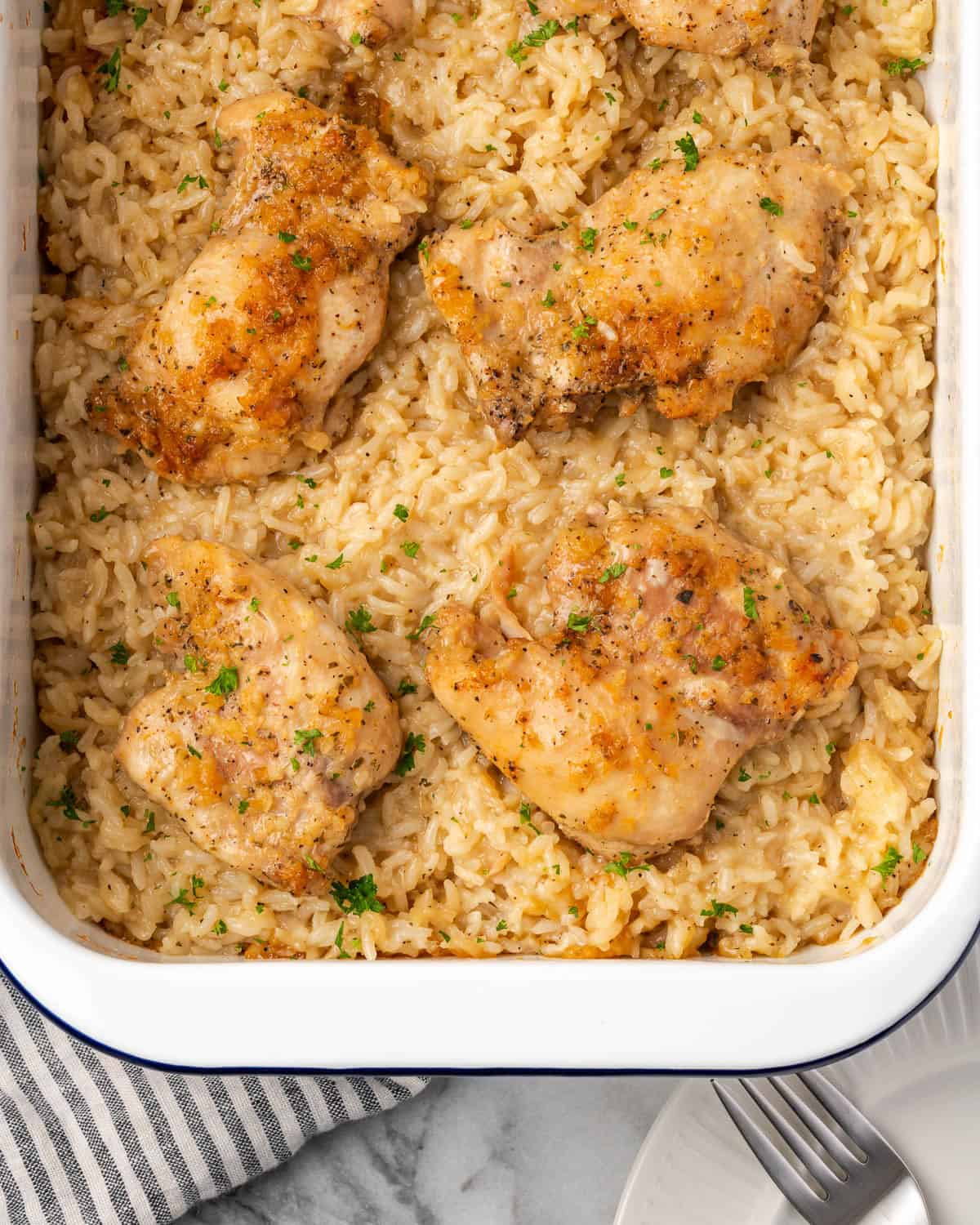 A casserole dish of baked chicken and rice sitting on a marble countertop. 