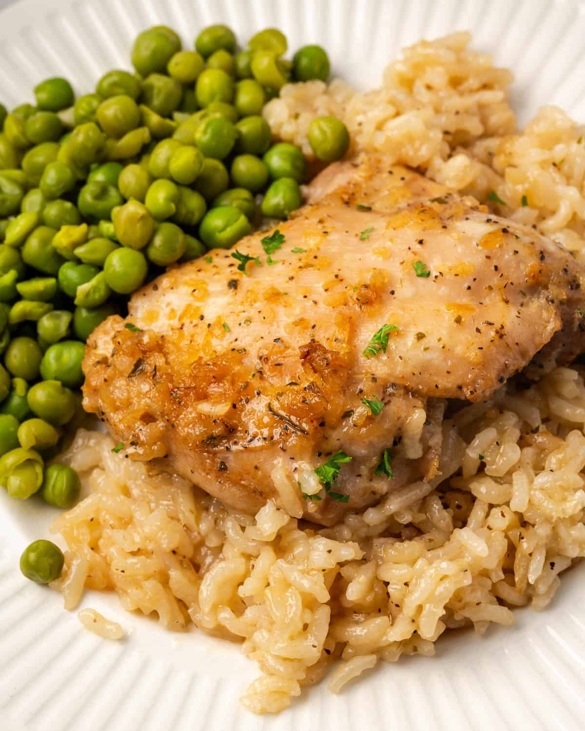 Baked chicken and rice served with a side of peas on a dinner plate.