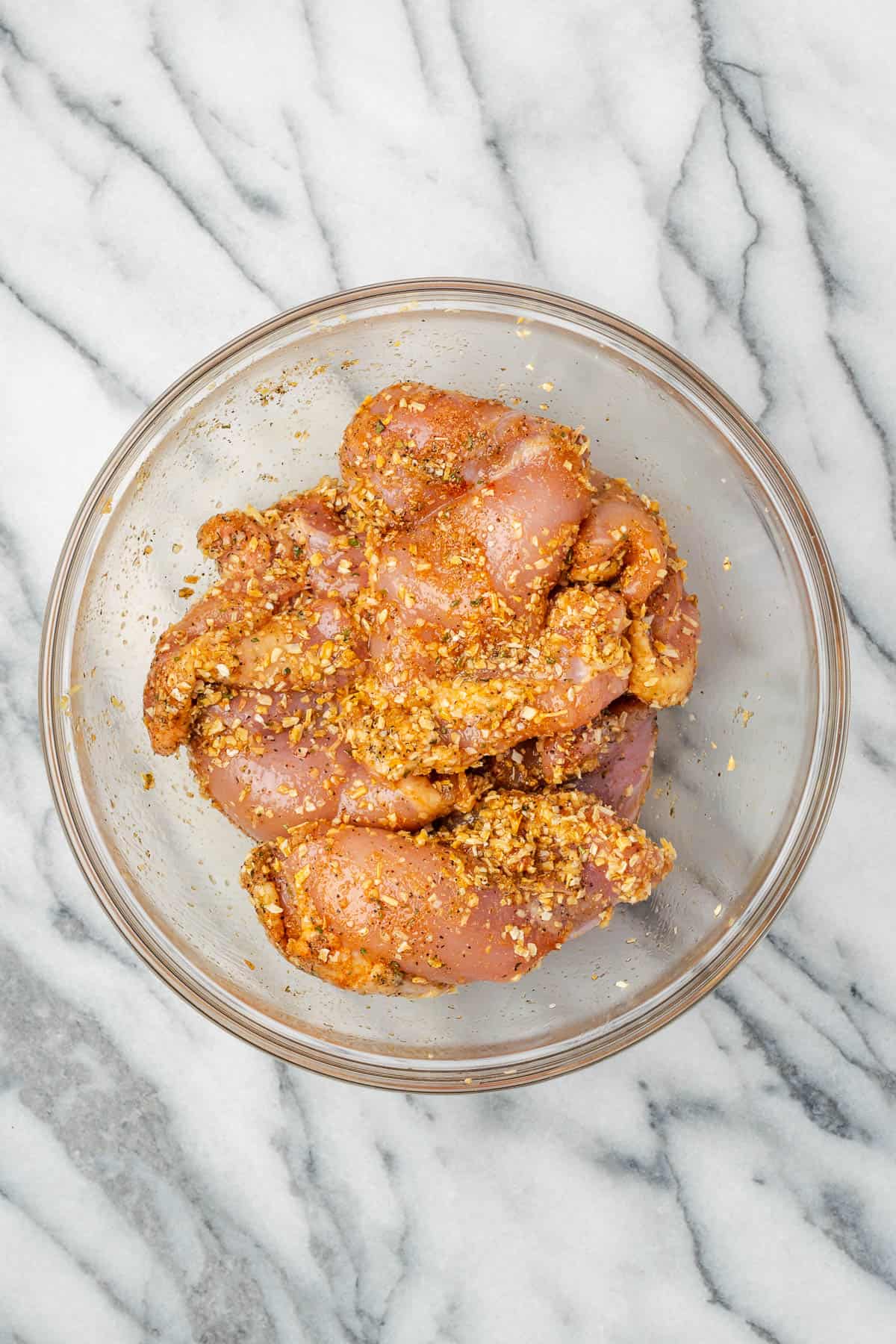 Seasoned chicken thighs in a large glass bowl. 