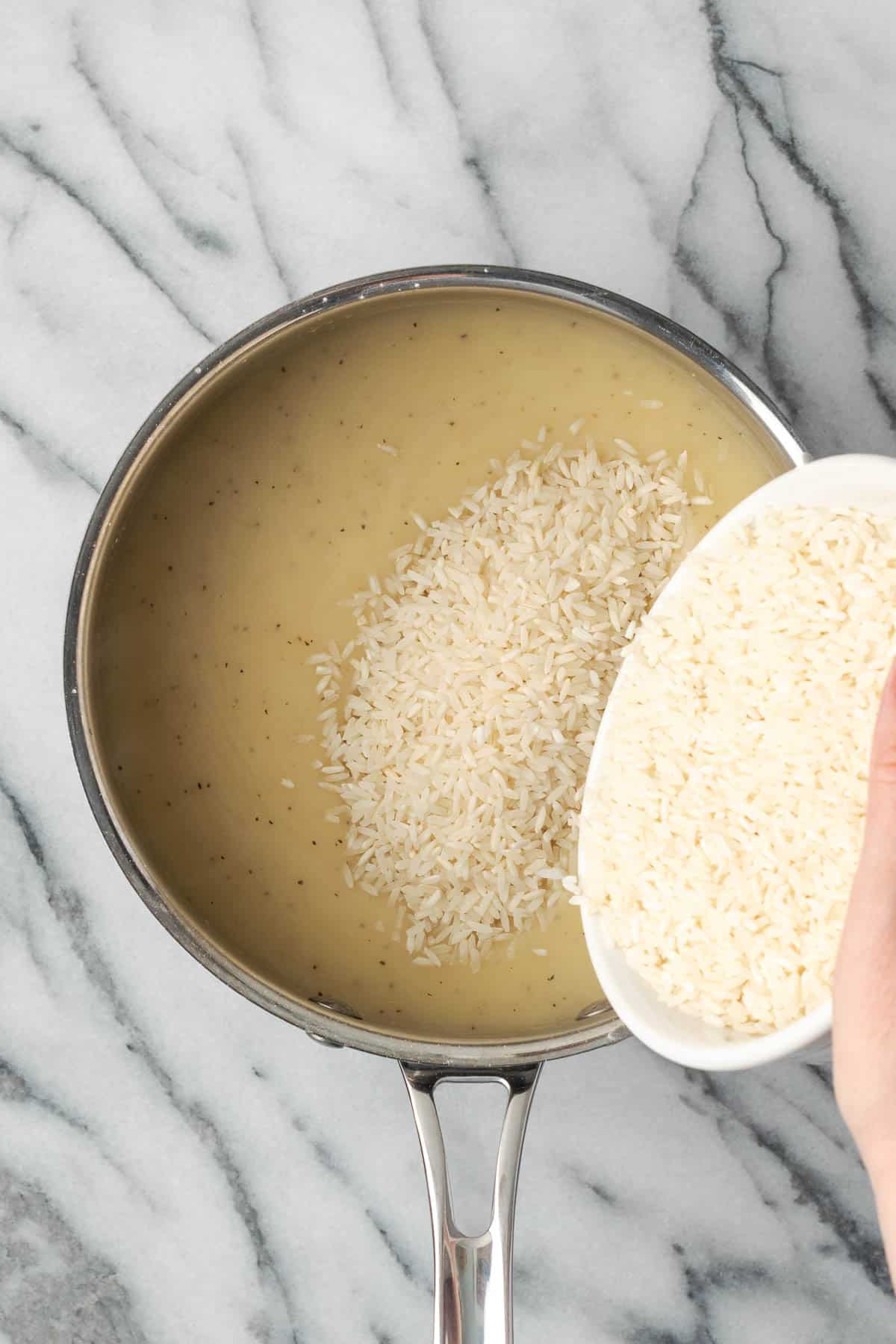 A bowl of rice being poured into the saucepan with the cream sauce.