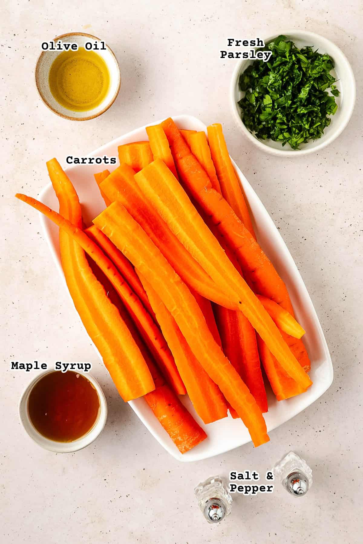Ingredients for oven roasted carrots with maple syrup sitting on a concrete counter.