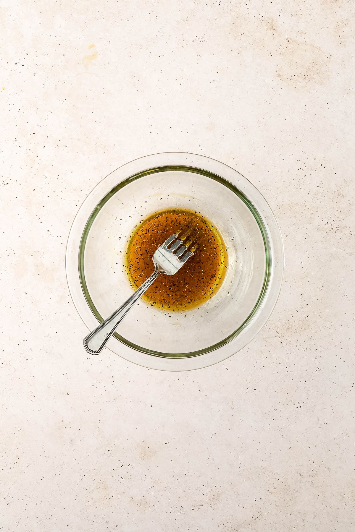 Olive oil, maple syrup, salt and pepper combined in a small glass bowl.