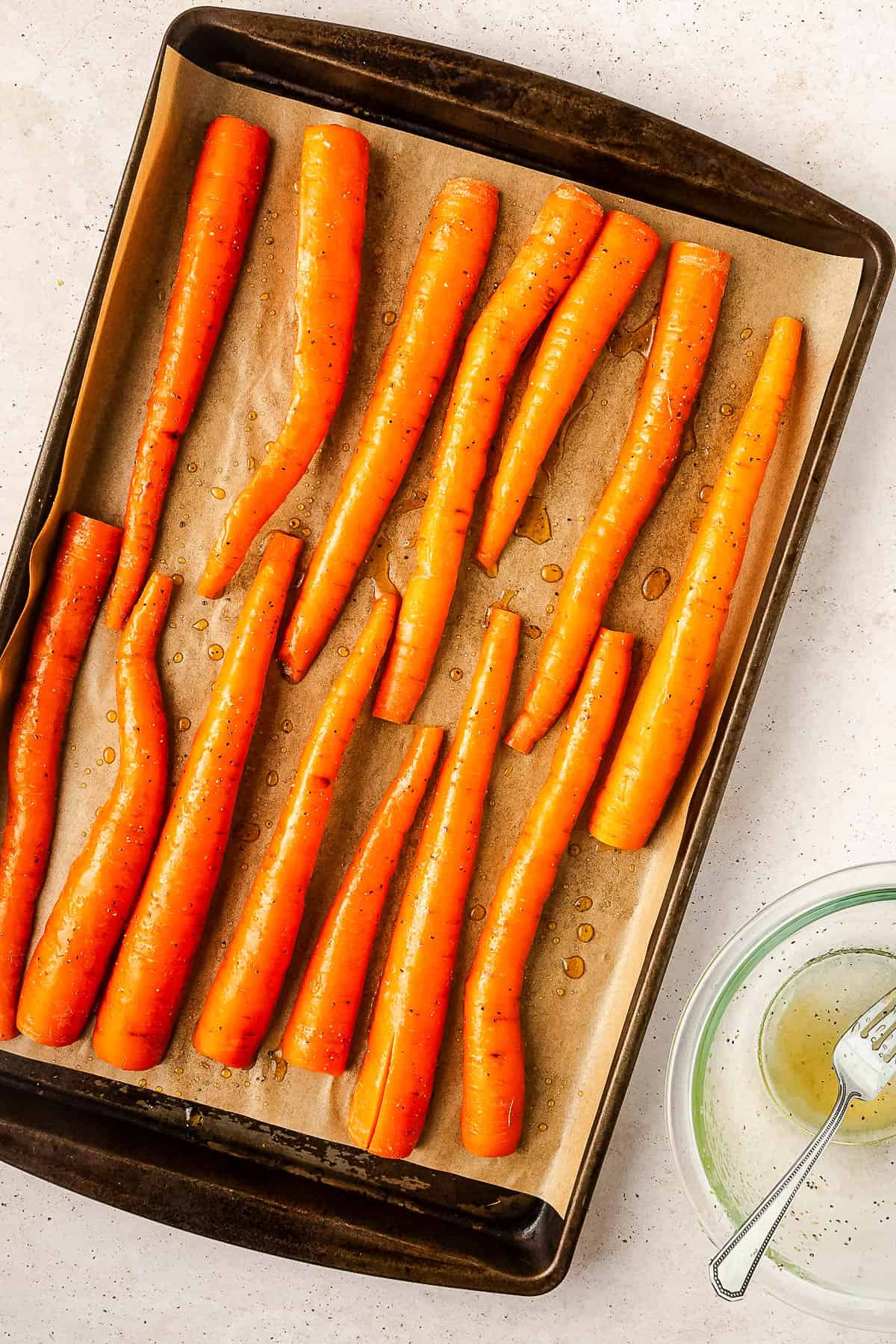 Unbaked glazed carrots laid out on a lined baking sheet.