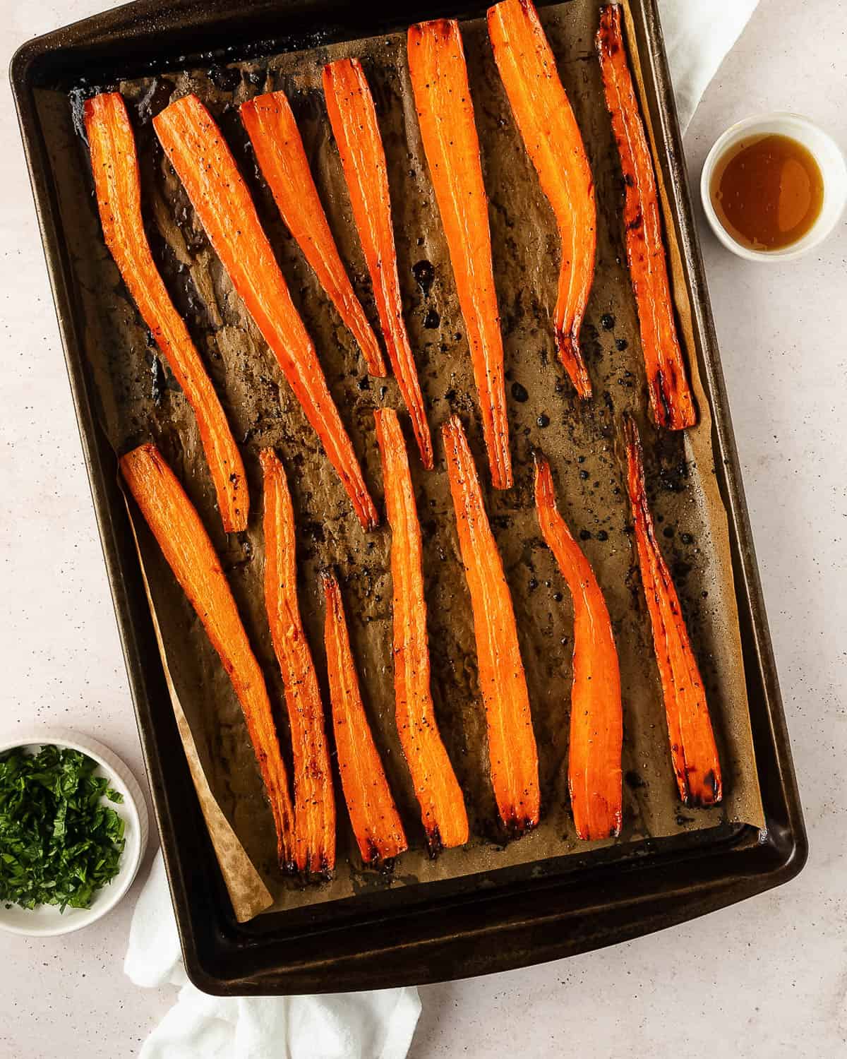 A baking pan with maple roasted carrots sitting next to a dish of fresh parsley.