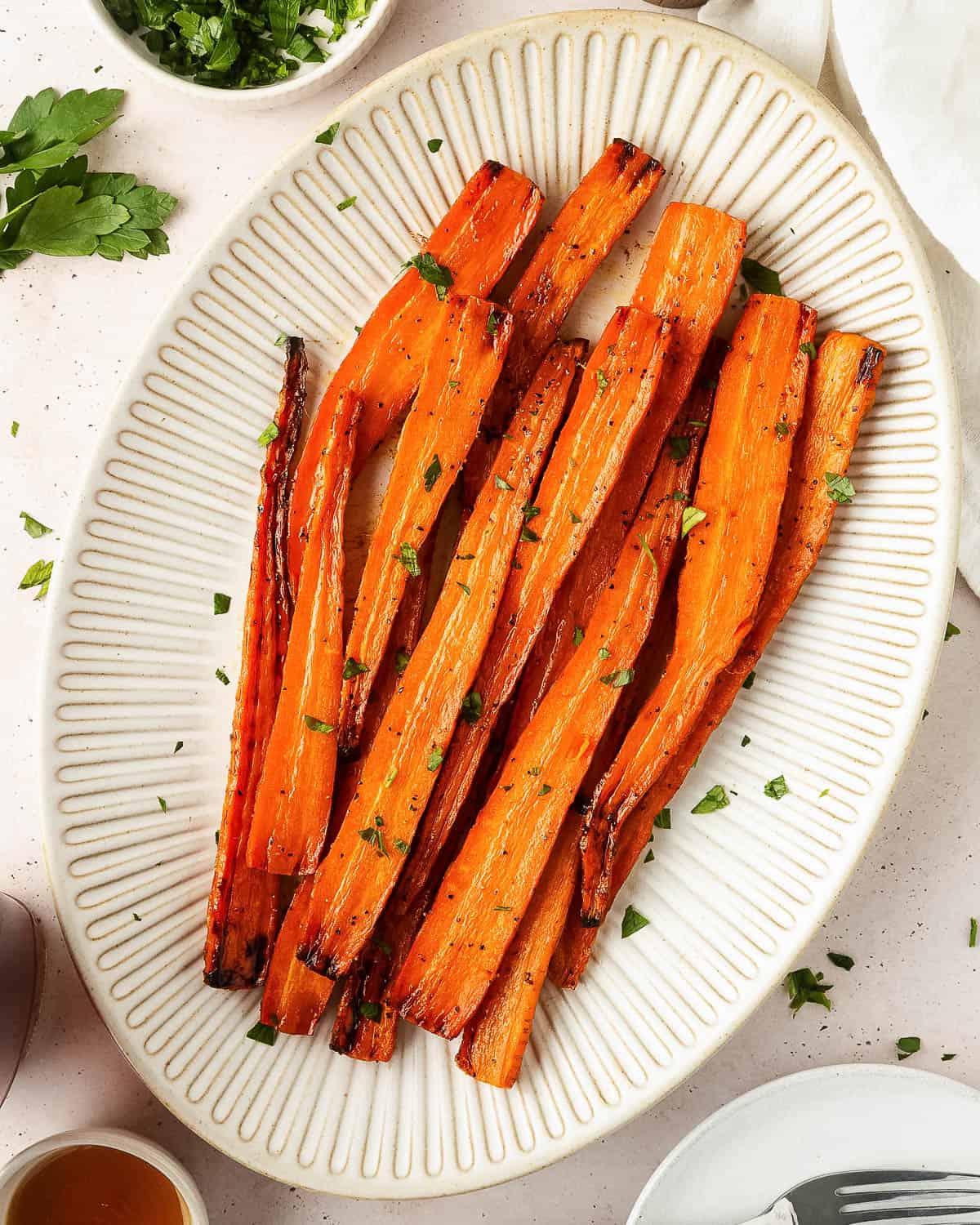 A serving platter of roasted carrots sprinkled with a little bit of fresh parsley.