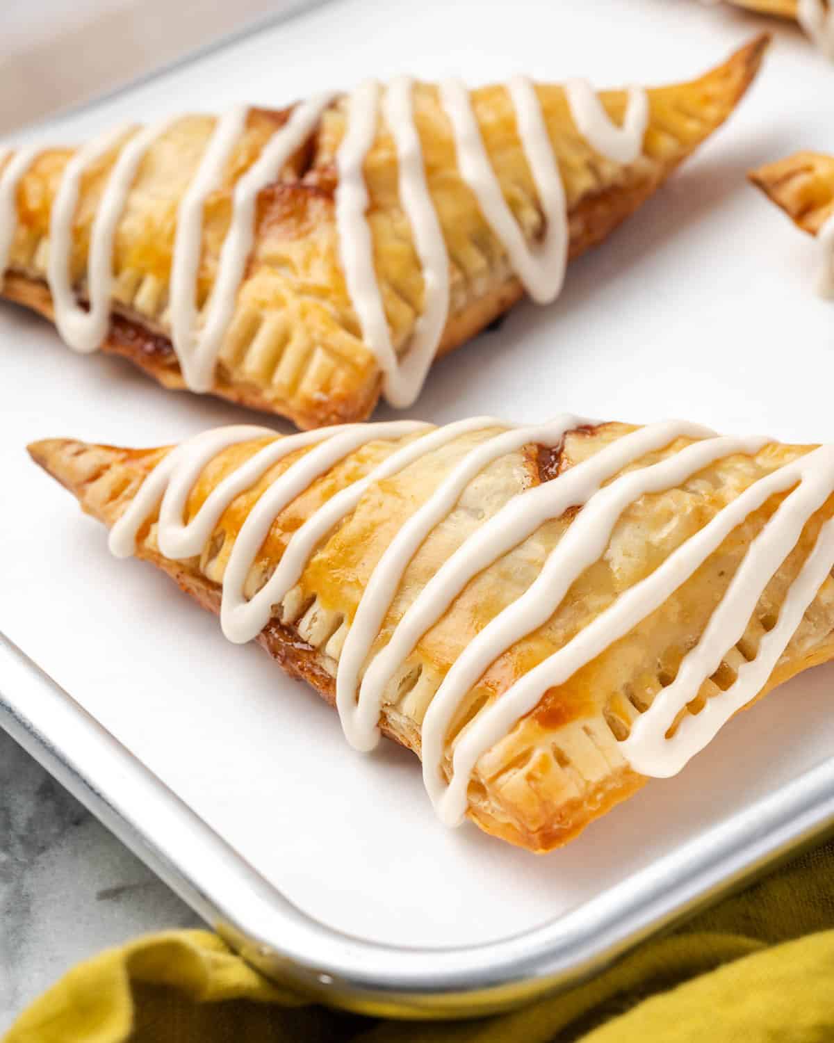Two apple turnovers made with puff pastry sitting on a metal tray. 