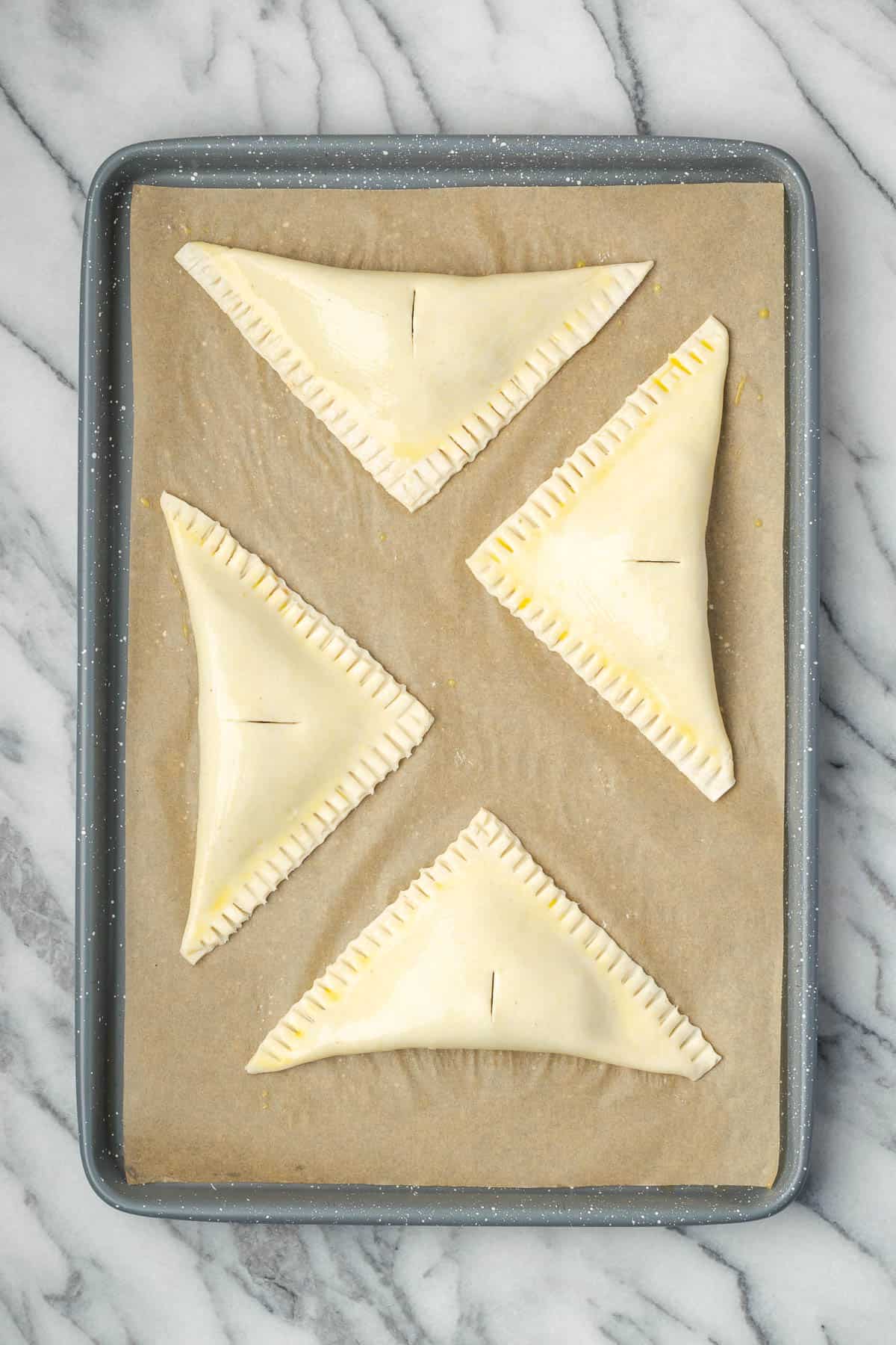 Four large apple turnovers sitting on a baking sheet. 