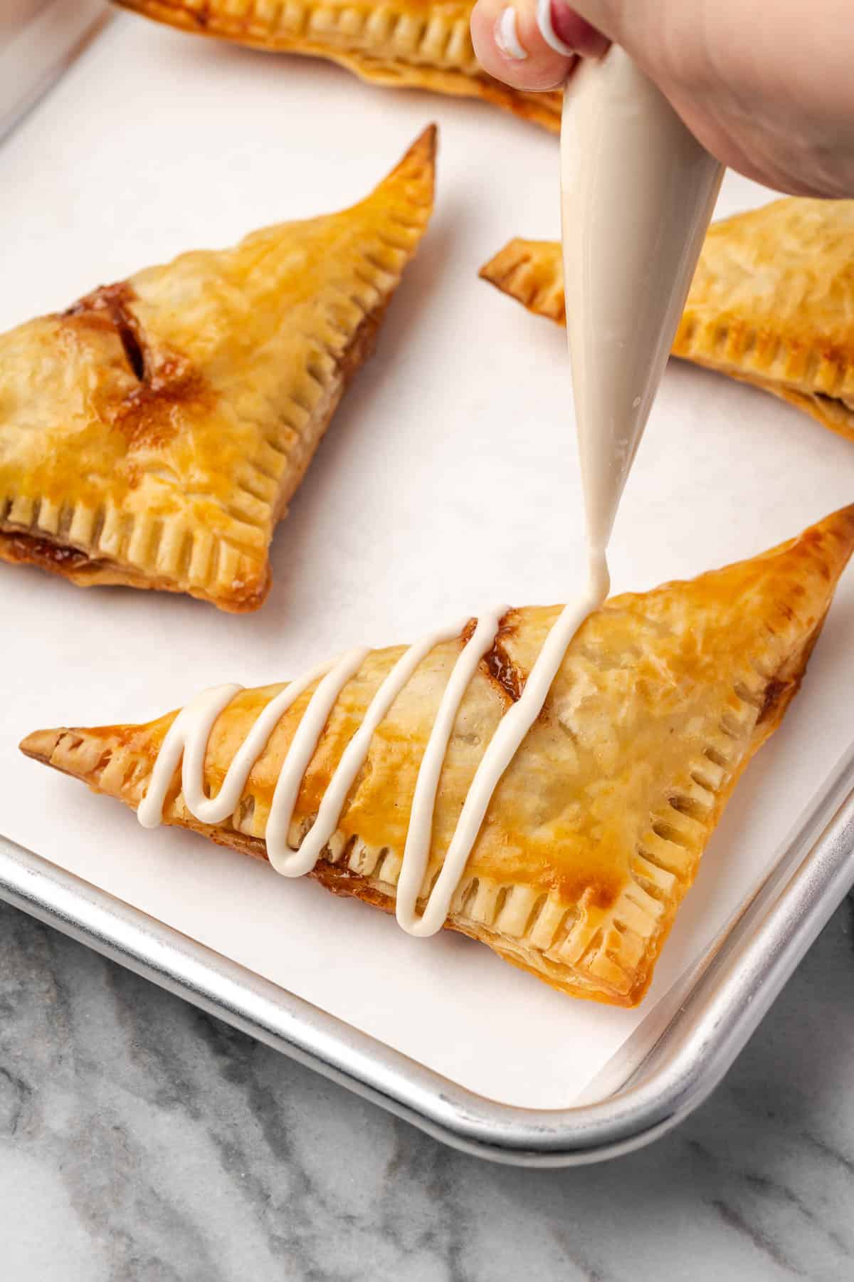 Icing being drizzled over freshly baked turnovers. 