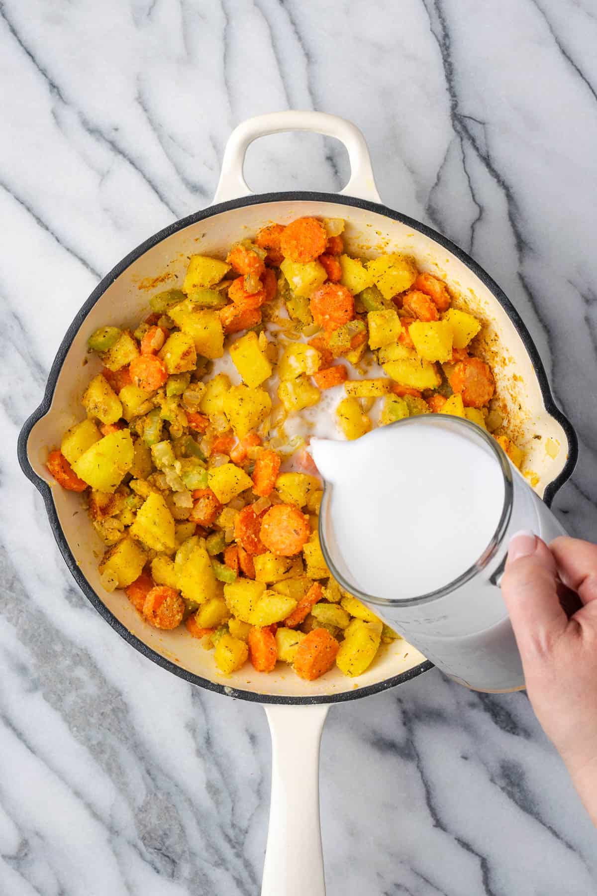 A measuring cup with milk being poured into the skillet with the vegetables.