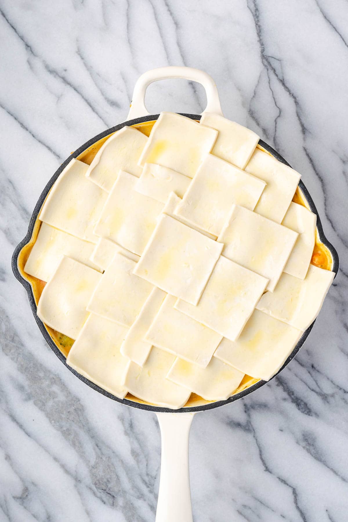 An unbaked veggie pot pie topped with a puff pastry crust sitting on a marble counter.
