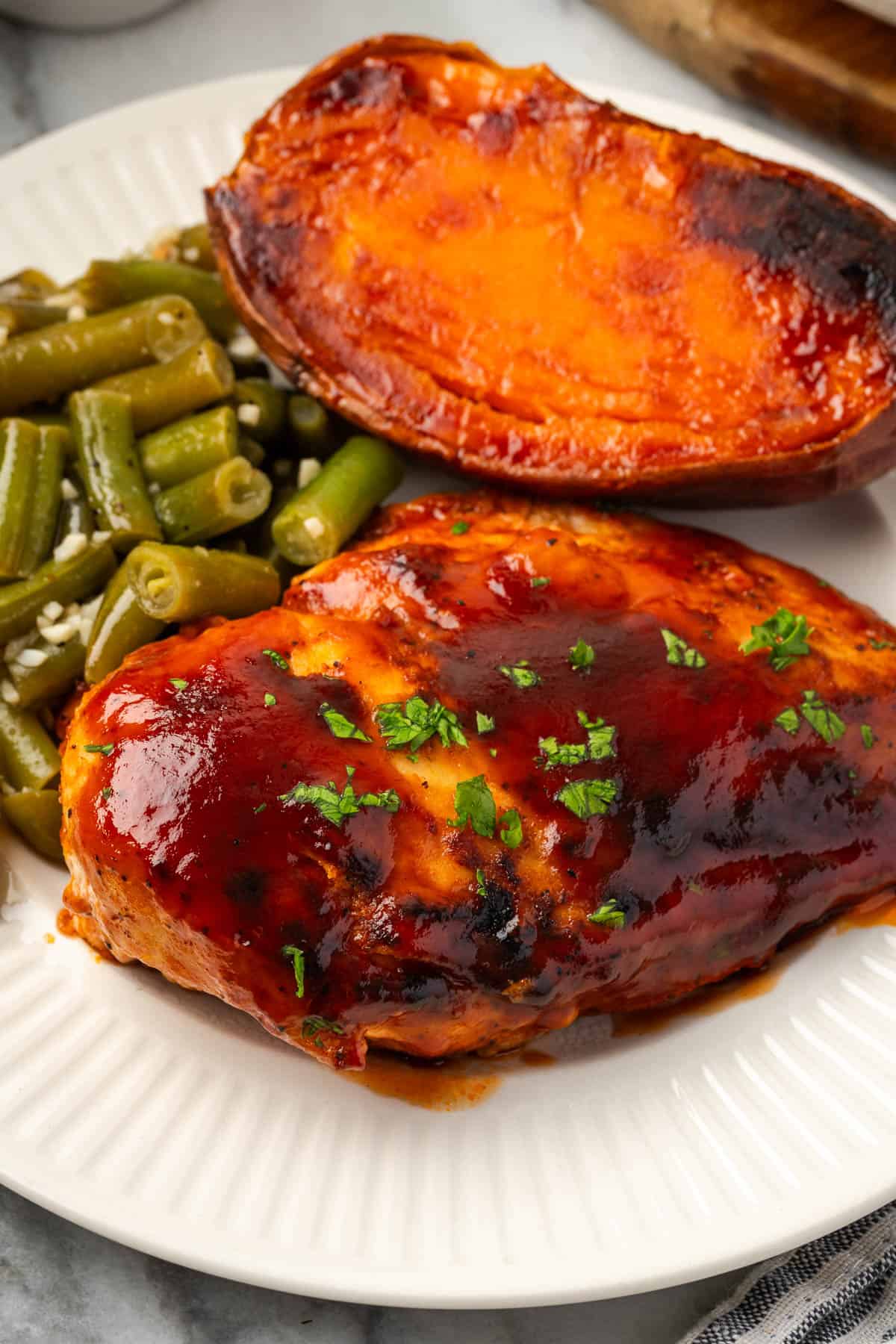 A dinner plate with a piece of bbq chicken, roasted sweet potato, and green beans. 