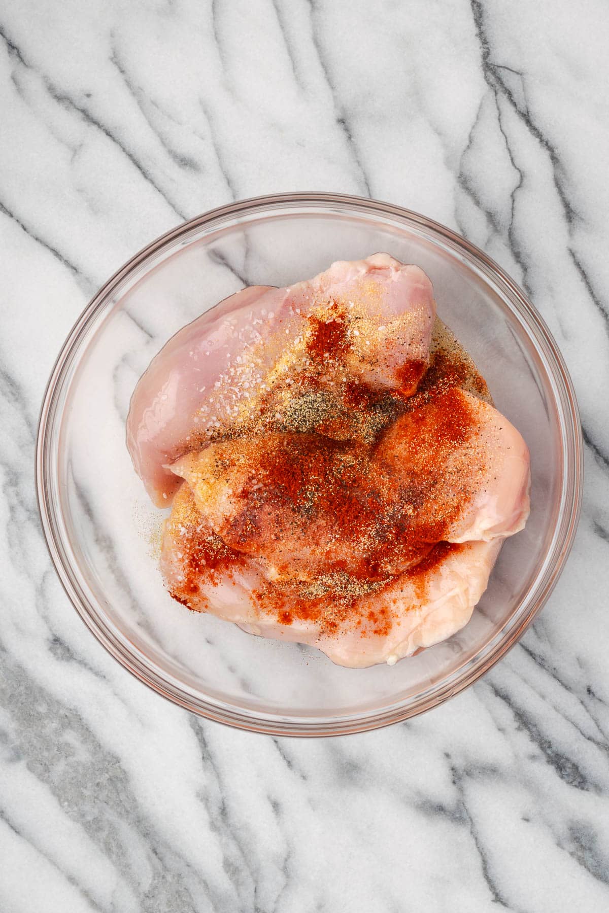 Raw chicken, olive oil, and spices combined in a large mixing bowl. 