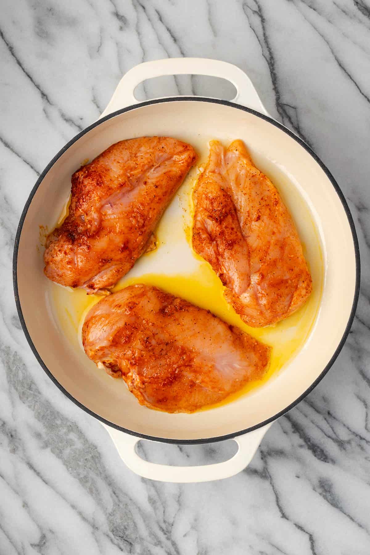 Three seasoned chicken breasts cooking in a skillet. 