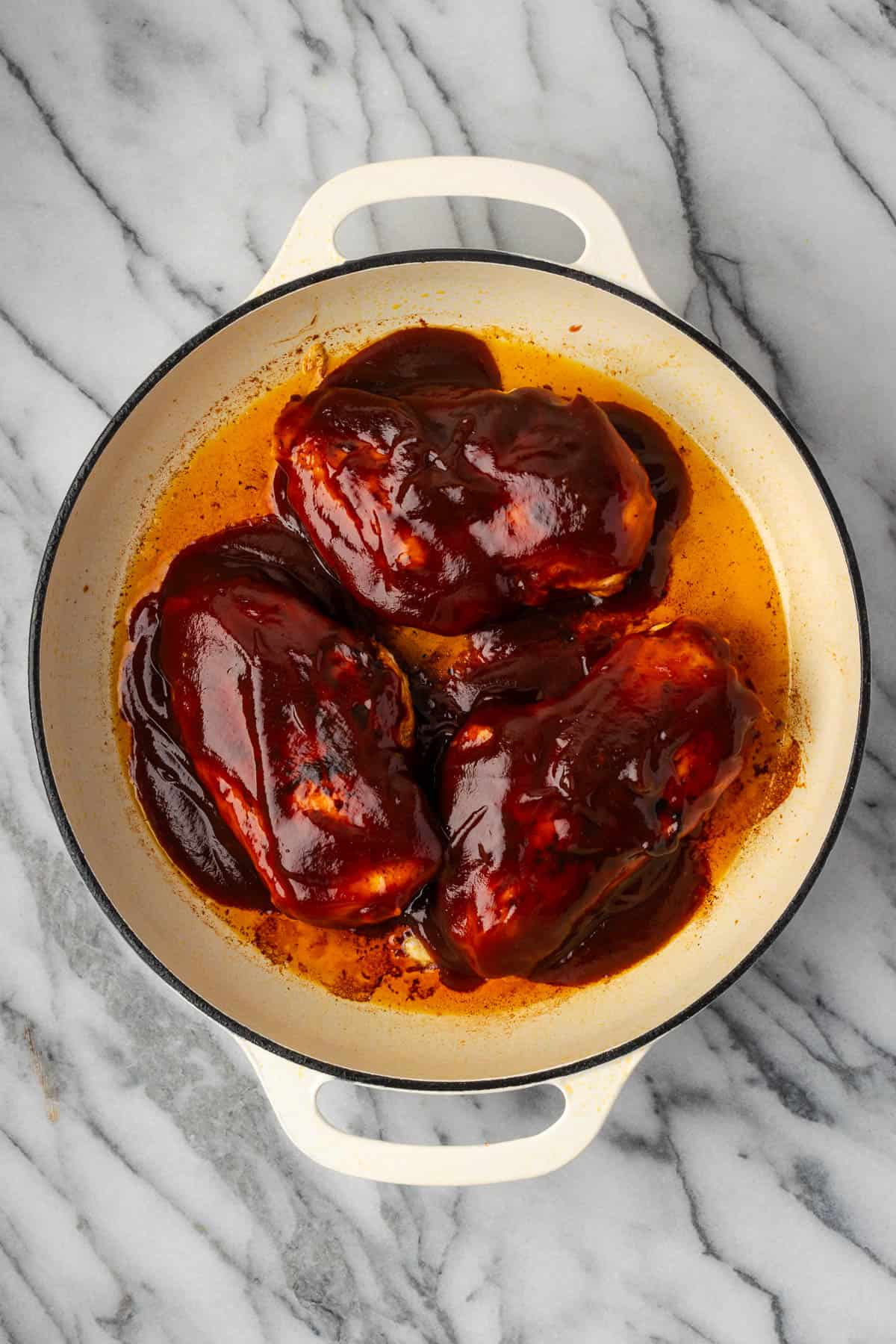 Partially cooked chicken with bbq sauce poured on top in a skillet. 