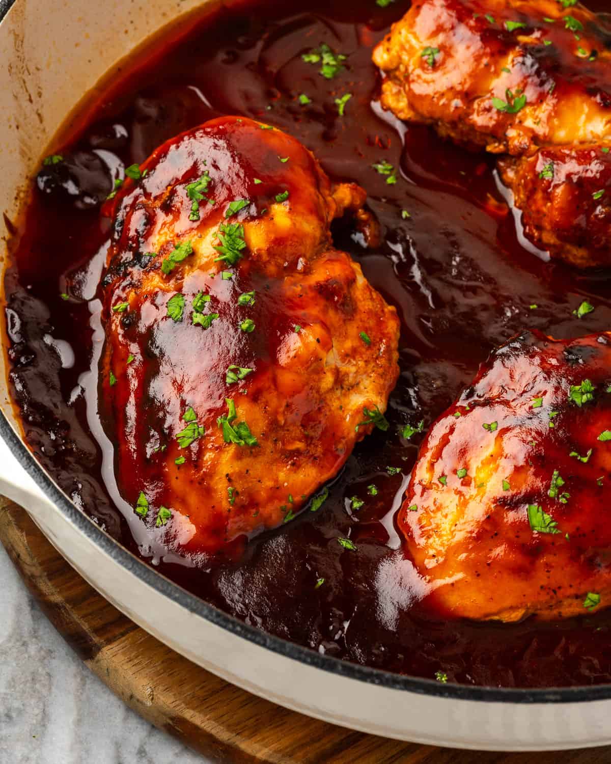 Baked barbecue chicken breasts in a cast iron pan sitting on a wood board.