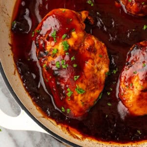 Several baked bbq chicken breasts in a cast iron pan.