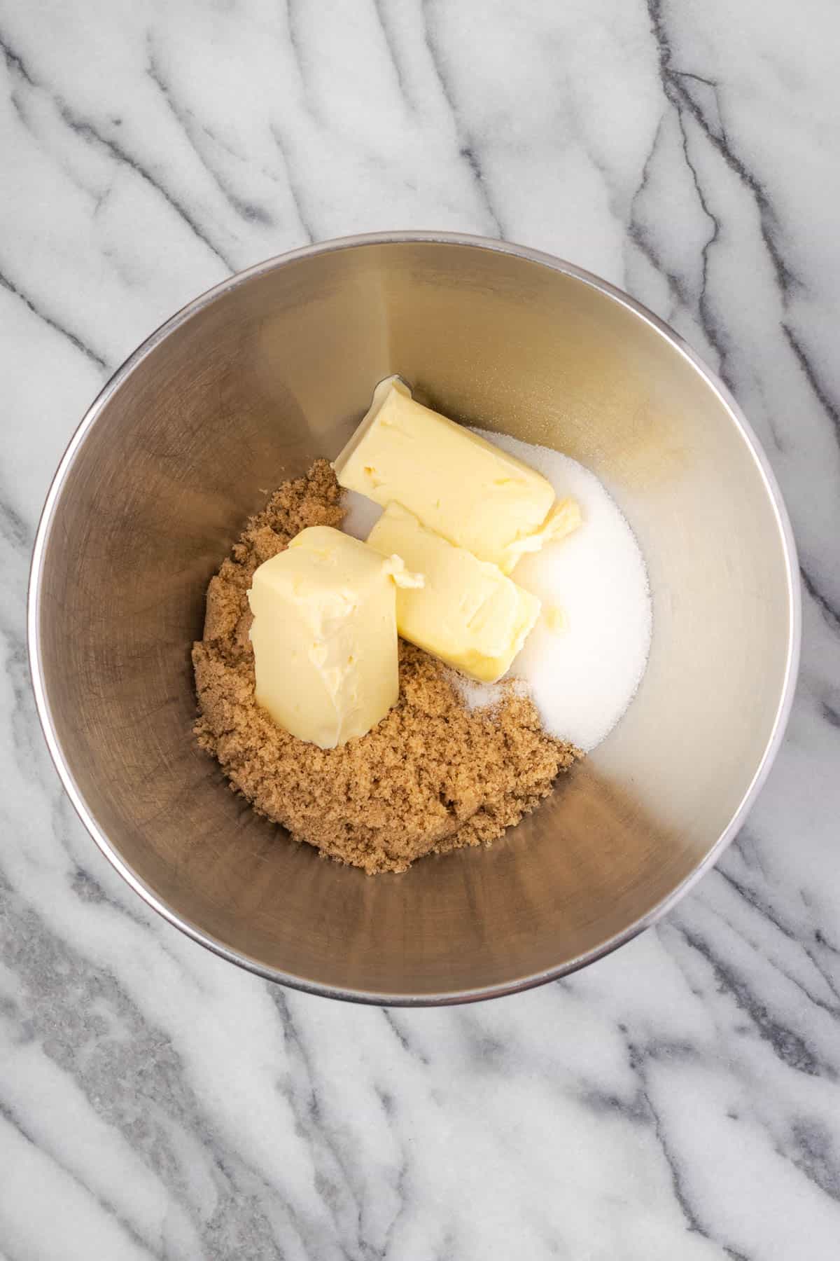 Brown sugar, sugar and butter combined in a large metal bowl. 