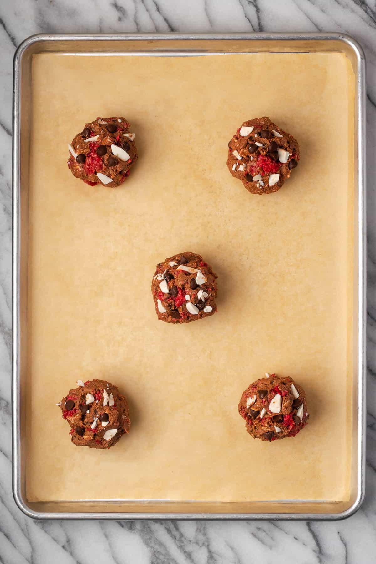 Five large balls of cookie dough on a baking sheet. 