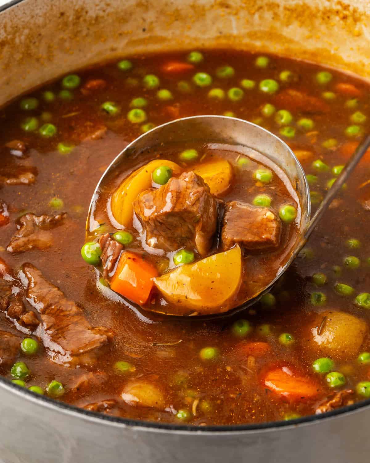 A ladle scooping beef stew from a Dutch oven pot.