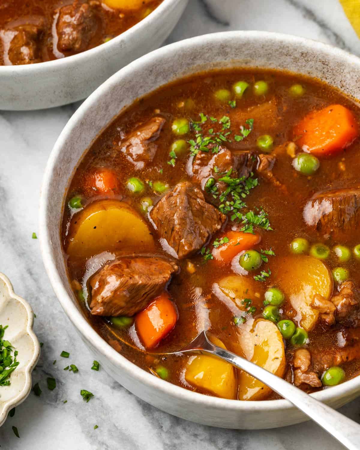 A spoon scooping a bite of beef stew from a ceramic bowl.