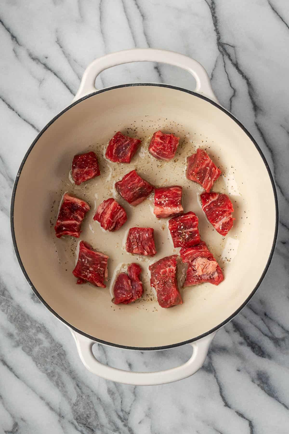Bite sized pieces of chuck roast cooking in a Dutch oven pot.