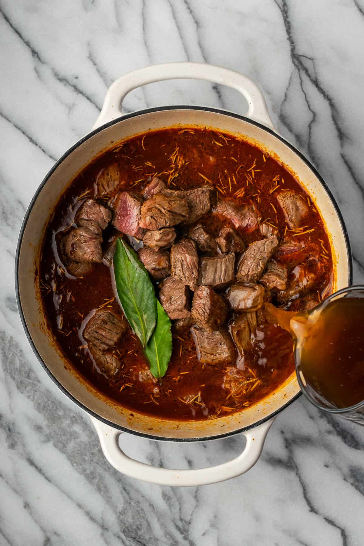 Cooked beef, beef broth and bay leaves are added to the pot.