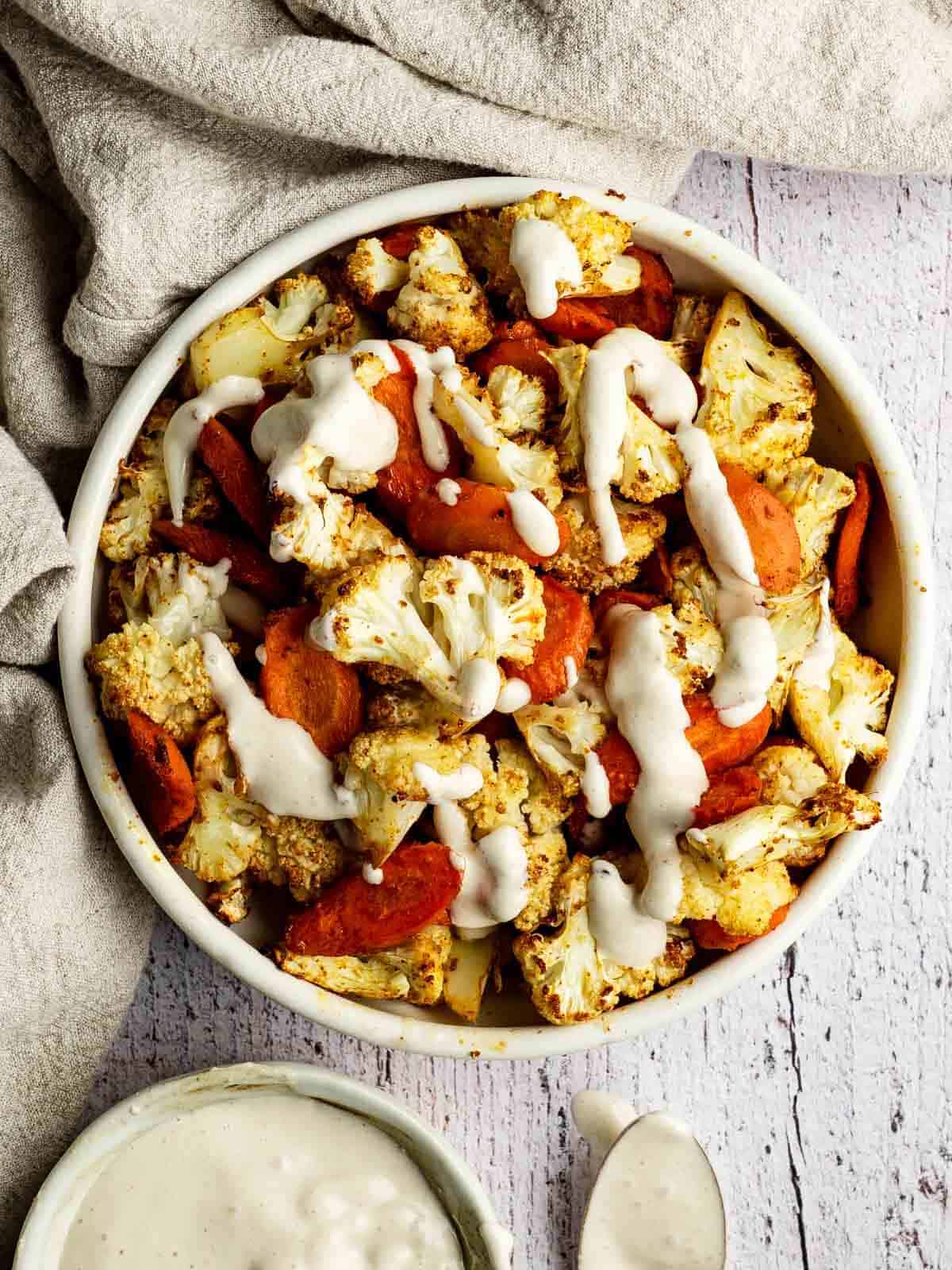 A bowl of carrots and cauliflower drizzled with white dressing.