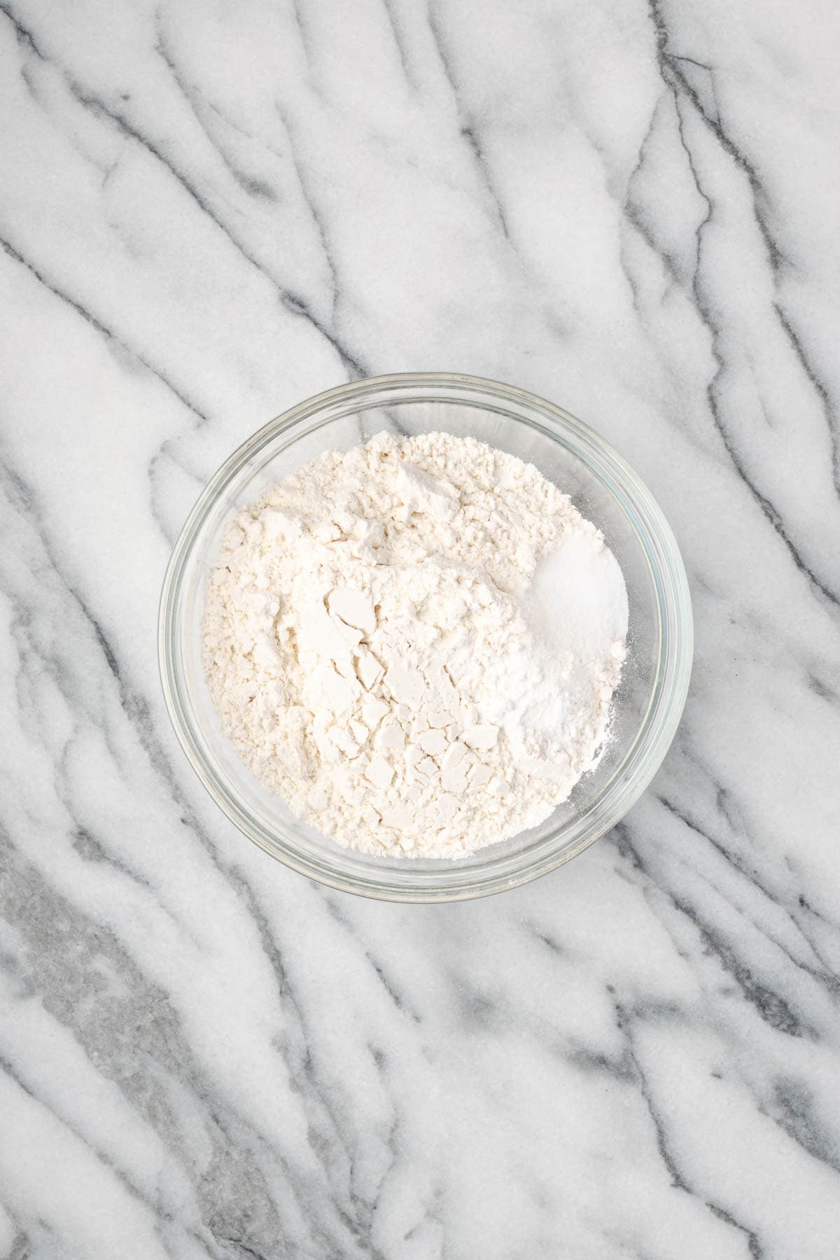 Flour, salt, and baking powder combined in a small glass bowl sitting on a marble counter.