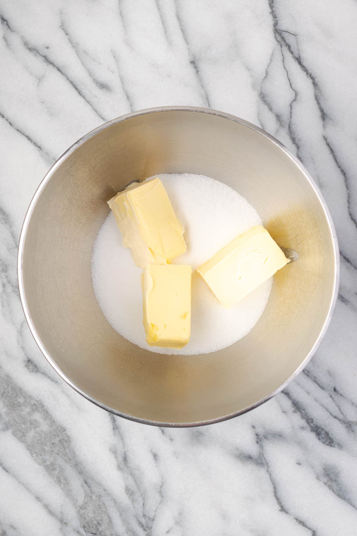 Butter and sugar combined in a large metal mixing bowl.