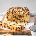 A loaf of chocolate chip pound cake cut into slices and sitting on a wood cutting board.