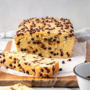 A loaf of chocolate chip pound cake cut into slices and sitting on a wood cutting board.