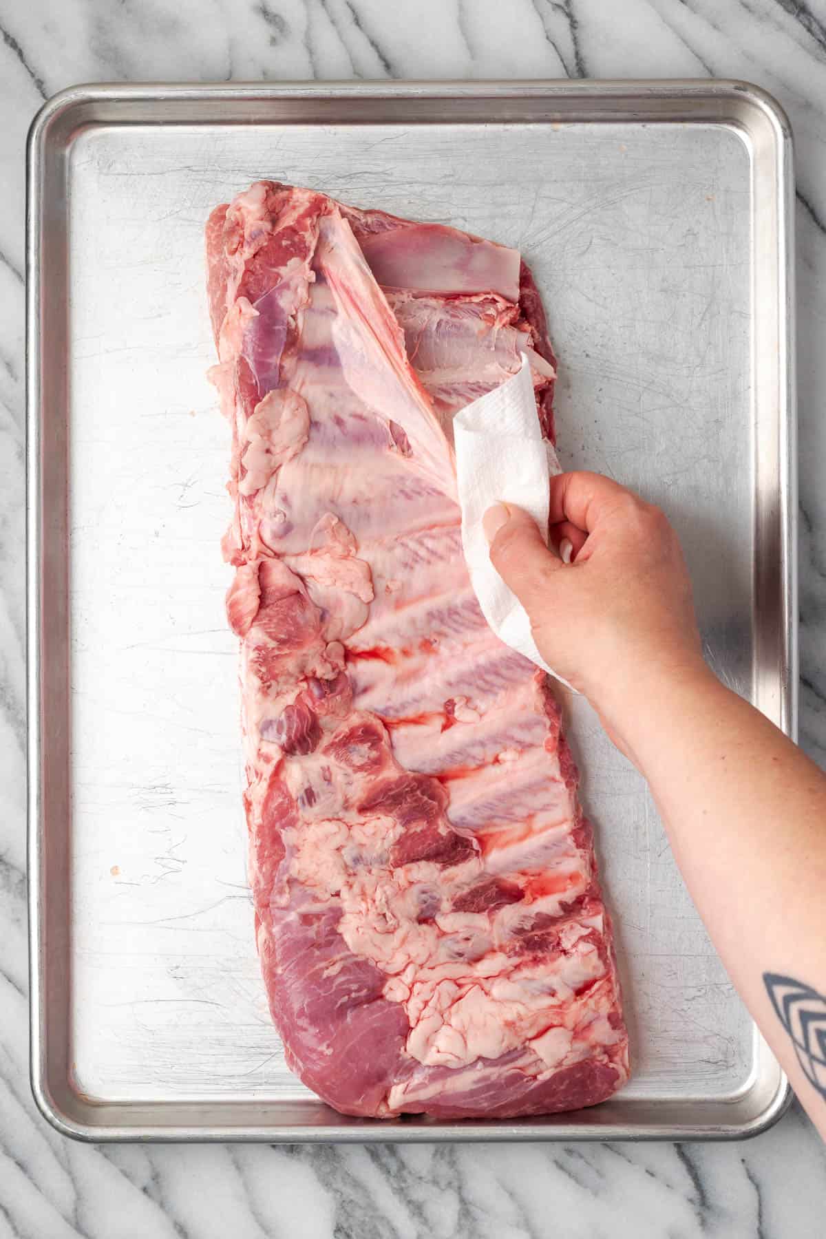The membrane being pulled off the underside of a rack of ribs.