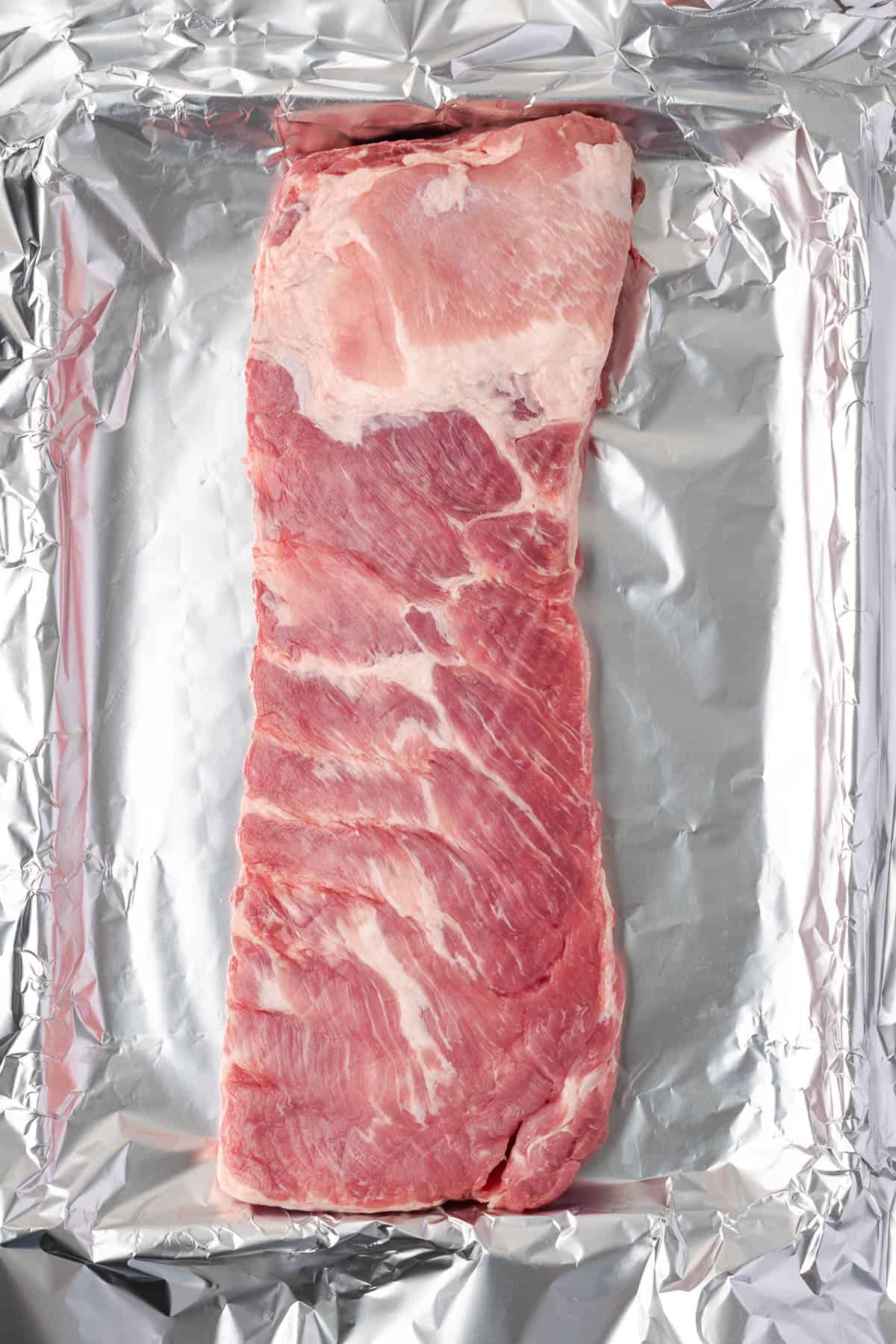 A rack of spareribs lying on a sheet of aluminum foil. 
