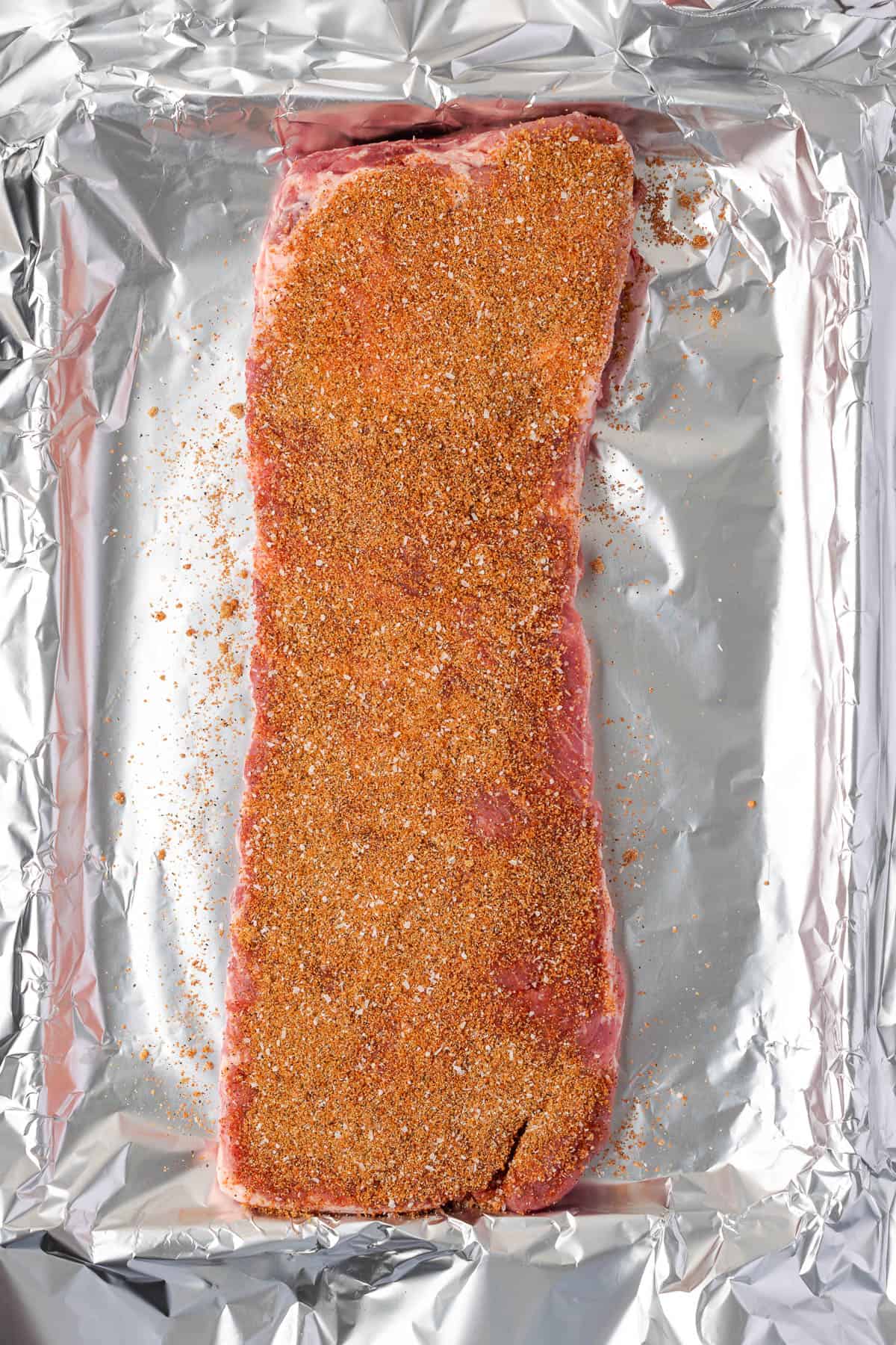 Pork ribs covered with a dry rub sitting on a baking sheet. 