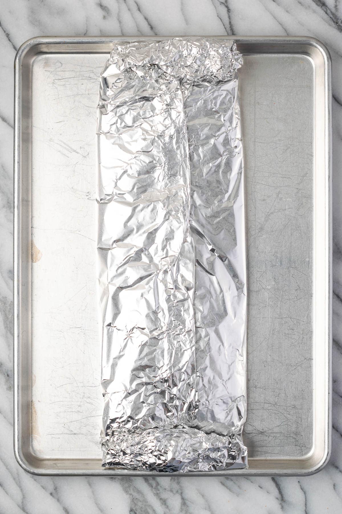 An unbaked rack of spareribs wrapped in aluminum foil. 