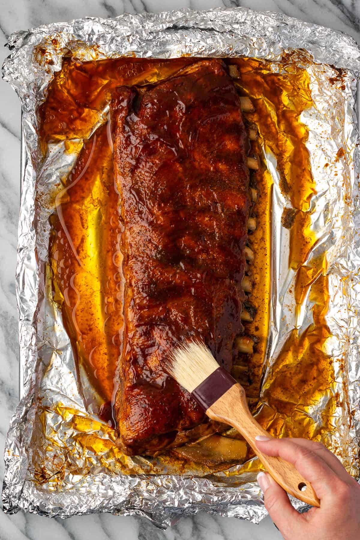 BBQ sauce being brushed onto baked ribs. 